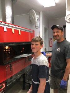 Smiling, standing by the pizza oven