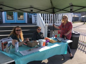 Three smiling volunteers staff the event table.